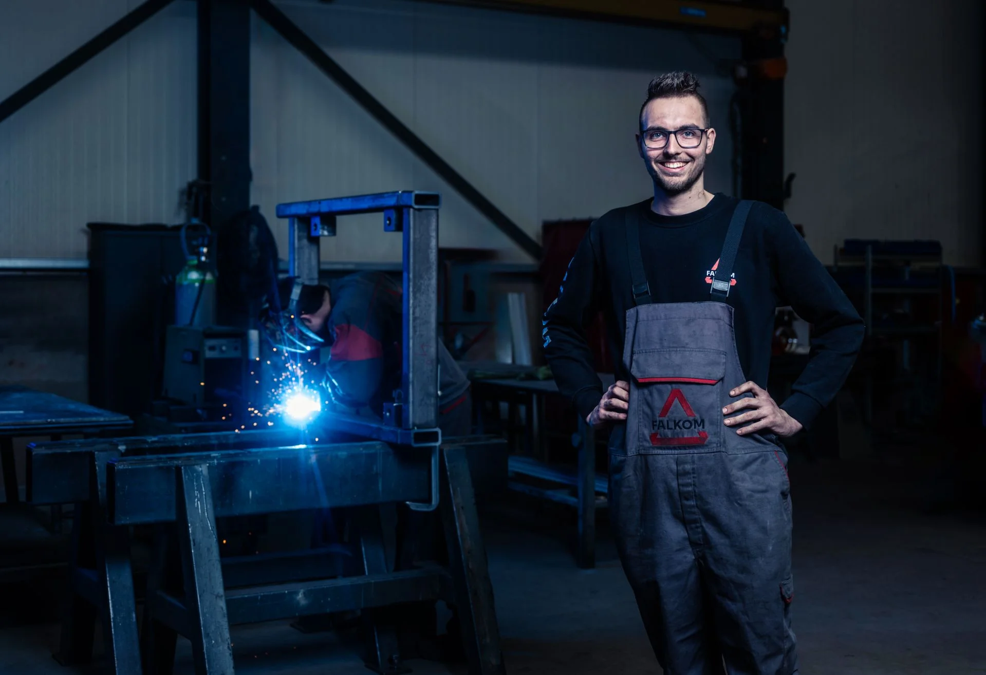 Medewerker van Falkom met laswerk in de werkplaats op de achtergrond.