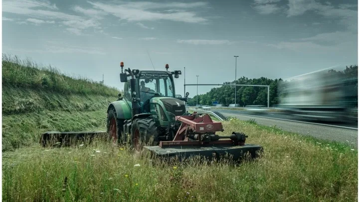 Trekker met maaiarm onderhoudt een berm langs de weg